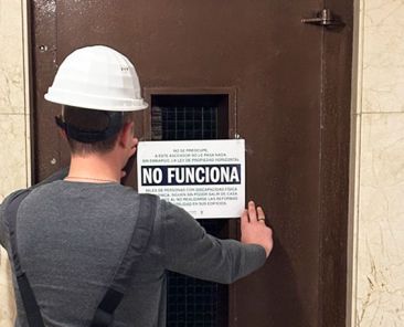 Un hombre coloca un cartel de 'No funciona' en un ascensor averiado.