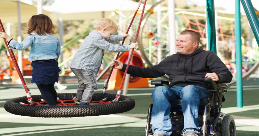 Un padre con discapacidad física junto a sus hijos en el parque