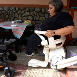 Persona en silla de ruedas trasladándose a una silla adaptada, en un entorno que refleja accesibilidad y mejoras en la movilidad para personas con discapacidad.