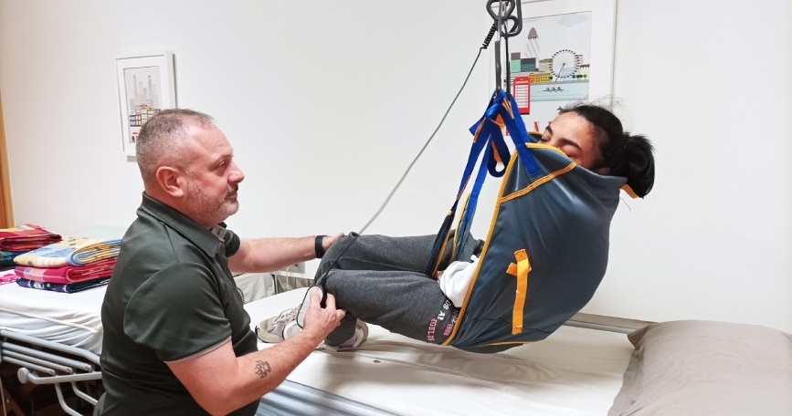 Auxiliar de geriatría ayudando a una usuaria en un centro de día, parte de un curso de formación