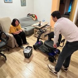 Persona con discapacidad en su hogar recibiendo una silla scooter como apoyo tras la DANA